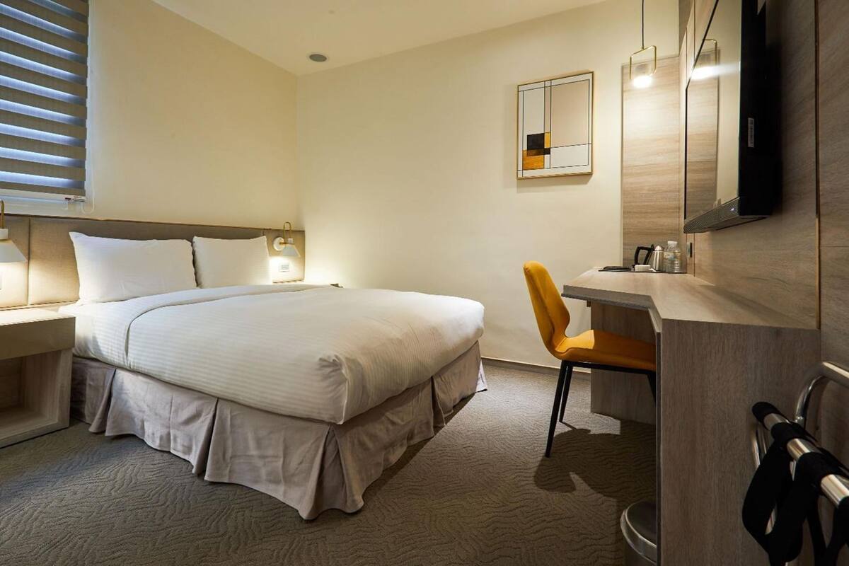Une chambre d’hôtel comprenant un lit, une table de chevet, une chaise, un bureau et un téléviseur.