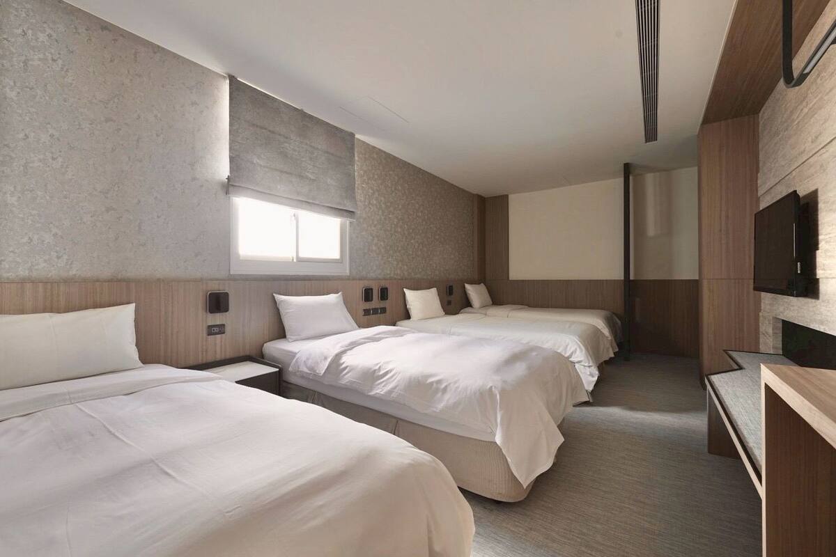 Une chambre d’hôtel avec trois lits, un téléviseur à écran plat et une grande fenêtre.