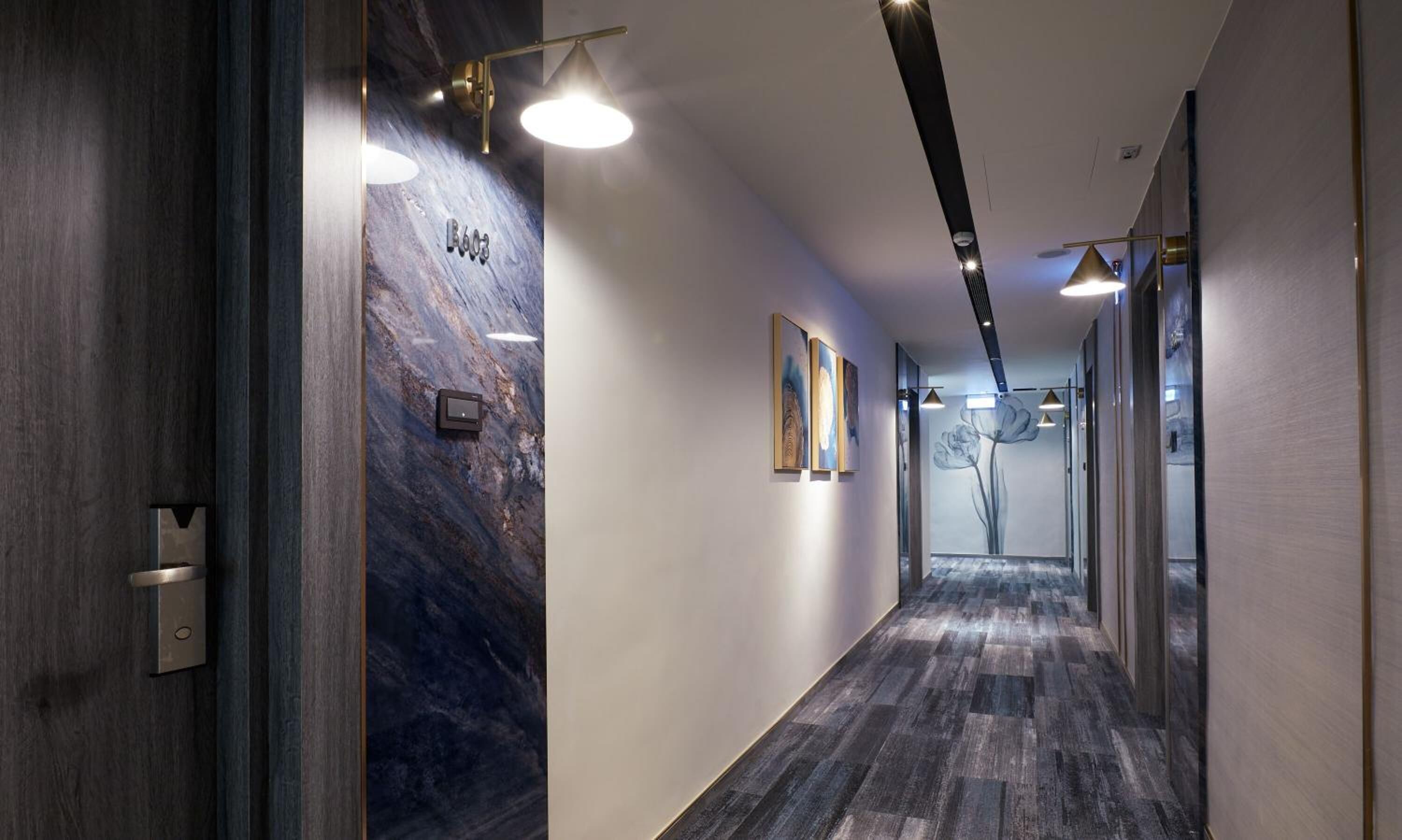 A modern hallway with a marble wall, recessed lighting, and a wooden floor.
