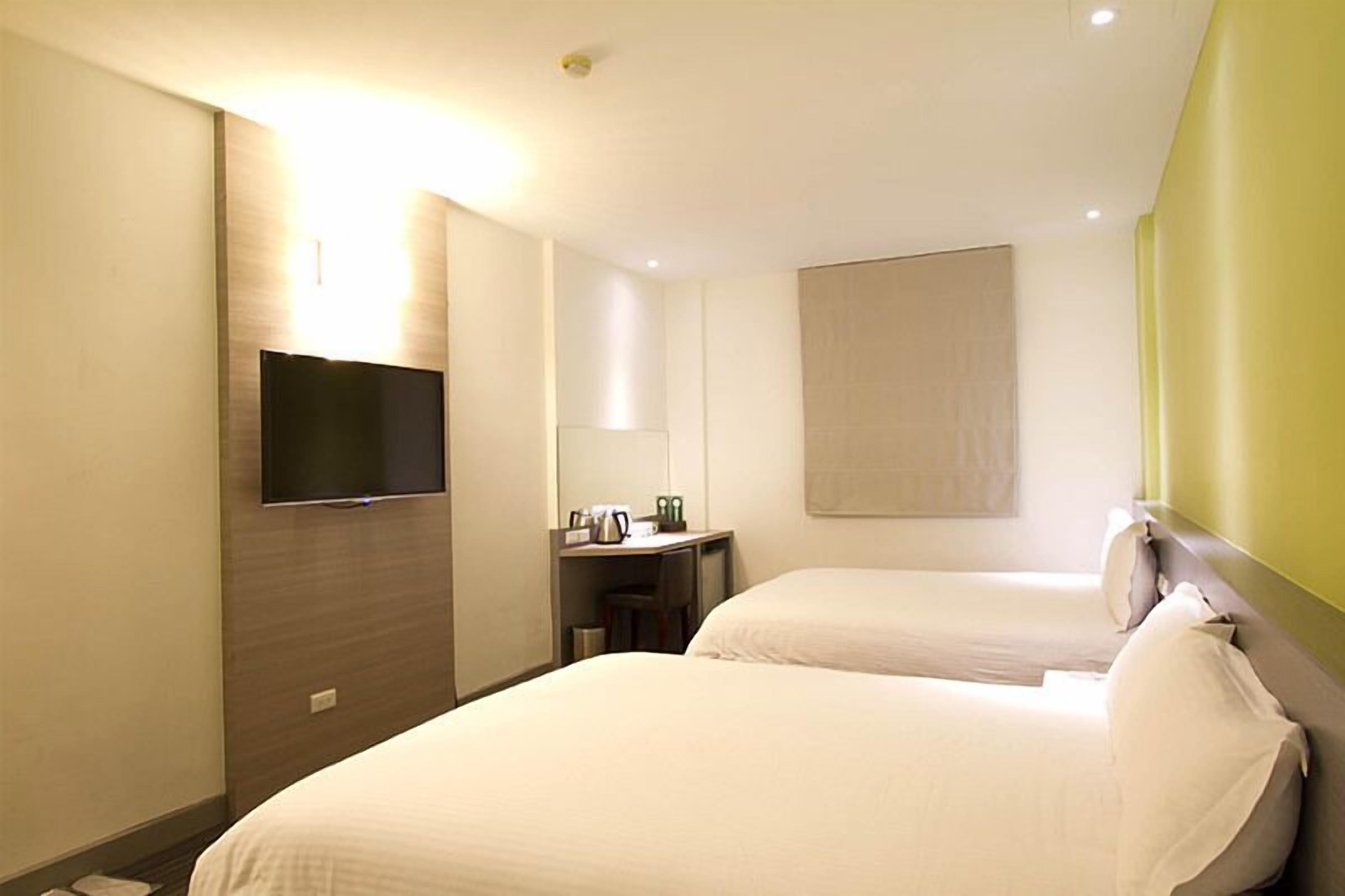 Habitació d'hotel amb dos llits, una televisió de pantalla plana penjada a la paret, un escriptori amb una cafetera i una finestra amb vistes.