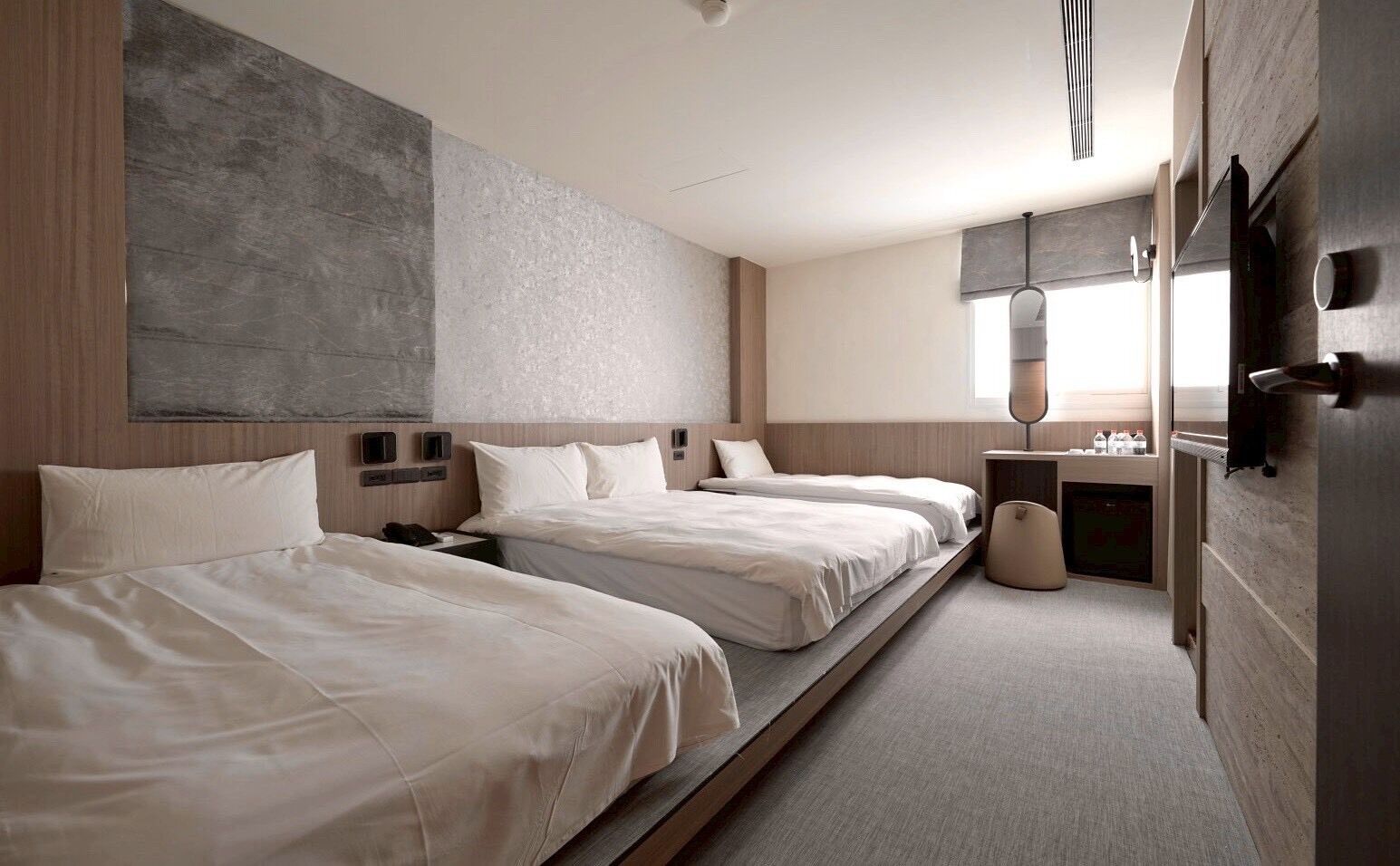 Ein Hotelzimmer mit zwei Betten, einem kleinen Schreibtisch, einem Spiegel und einem Fenster.