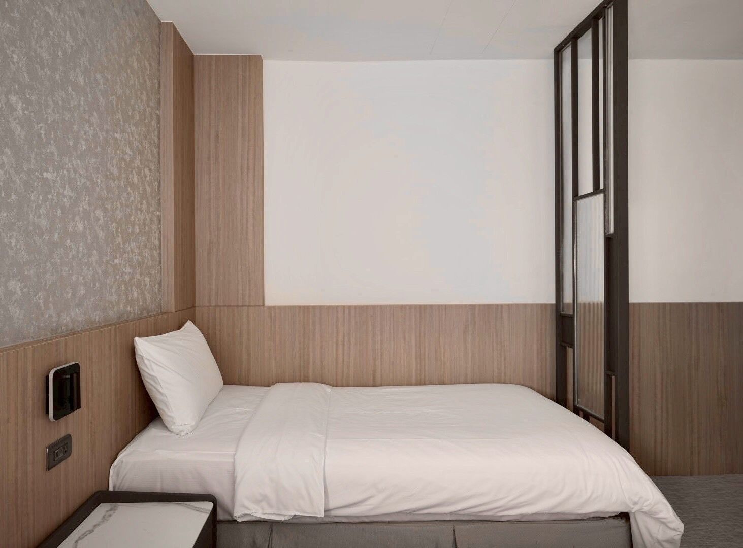 A modern hotel room with a bed, a bedside table, and a large window.