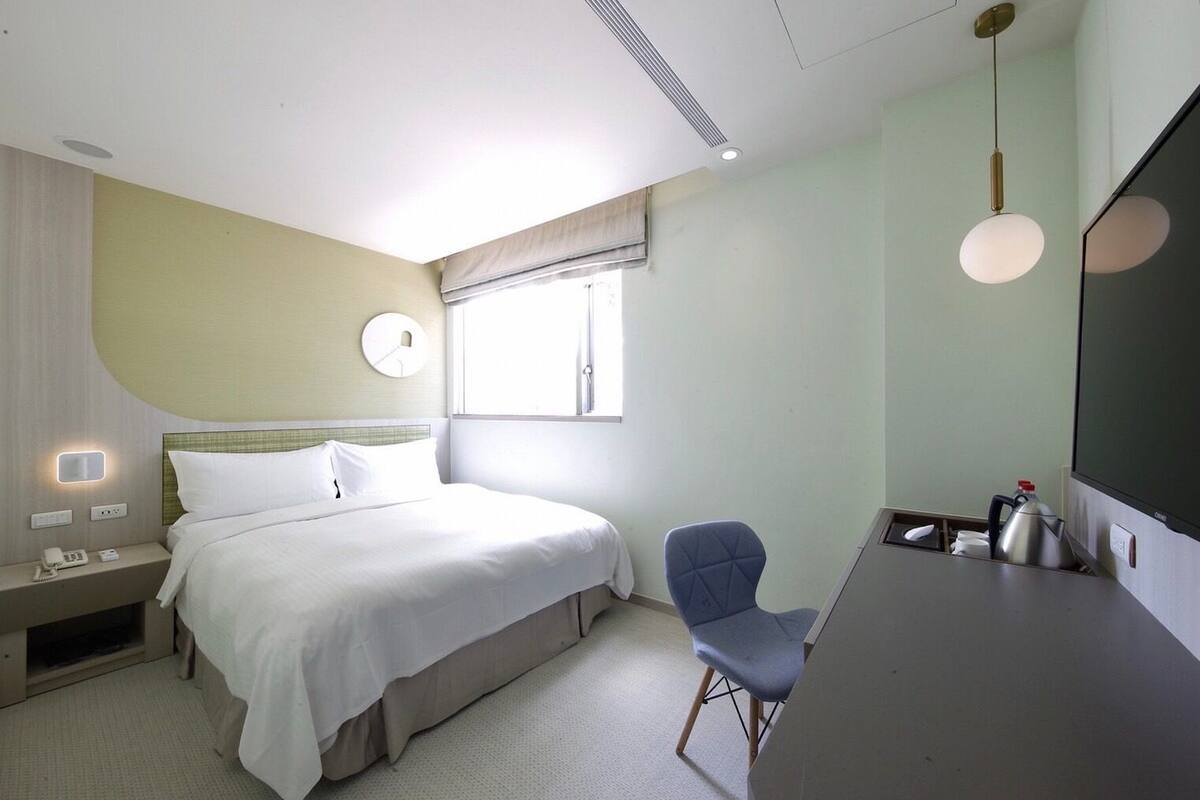 Une chambre d’hôtel équipée d’un lit, d’une table de chevet, d’une chaise et d’un bureau avec une bouilloire.