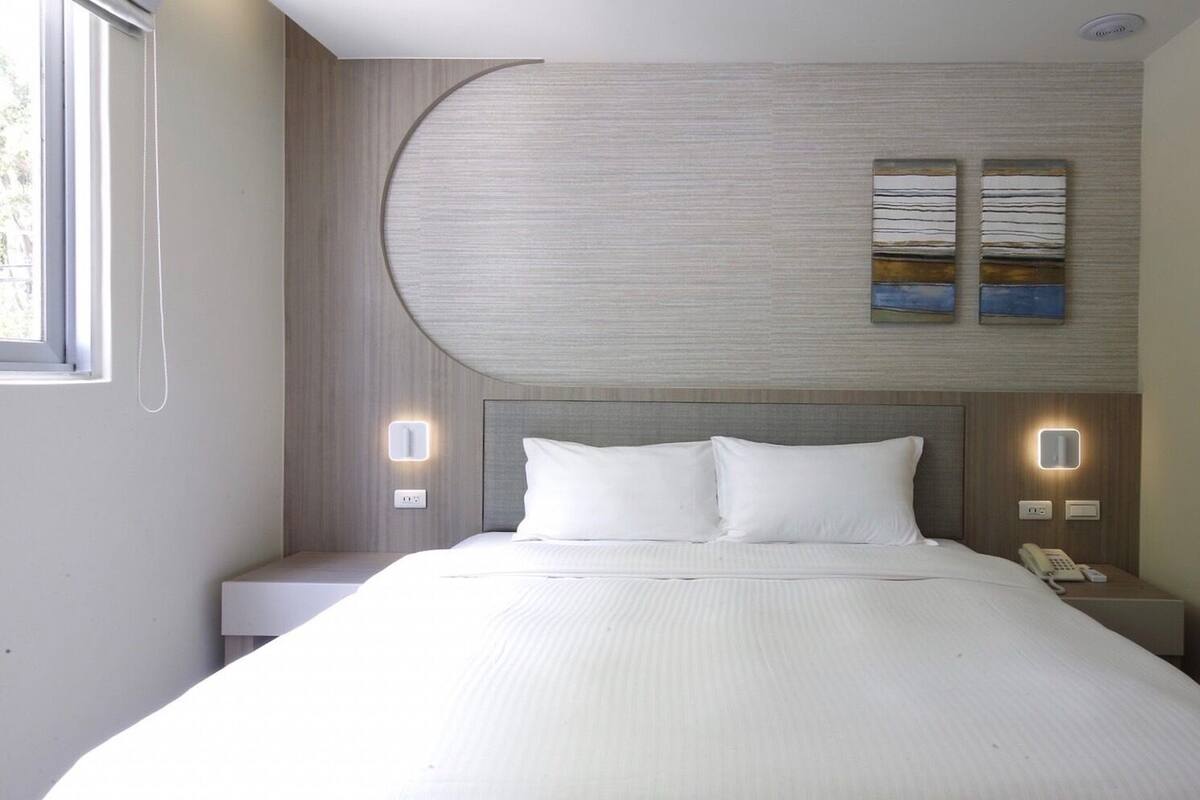 Une chambre d’hôtel moderne avec un grand lit, deux tables de chevet avec des lampes et un mur au design incurvé.