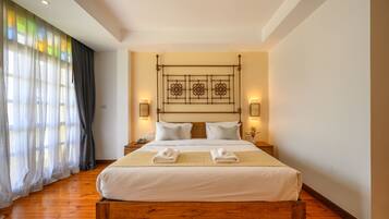Un lit bien fait, avec du linge de lit blanc et deux serviettes, une tête de lit en bois ornée d’un motif décoratif et deux lampes fixées au mur.