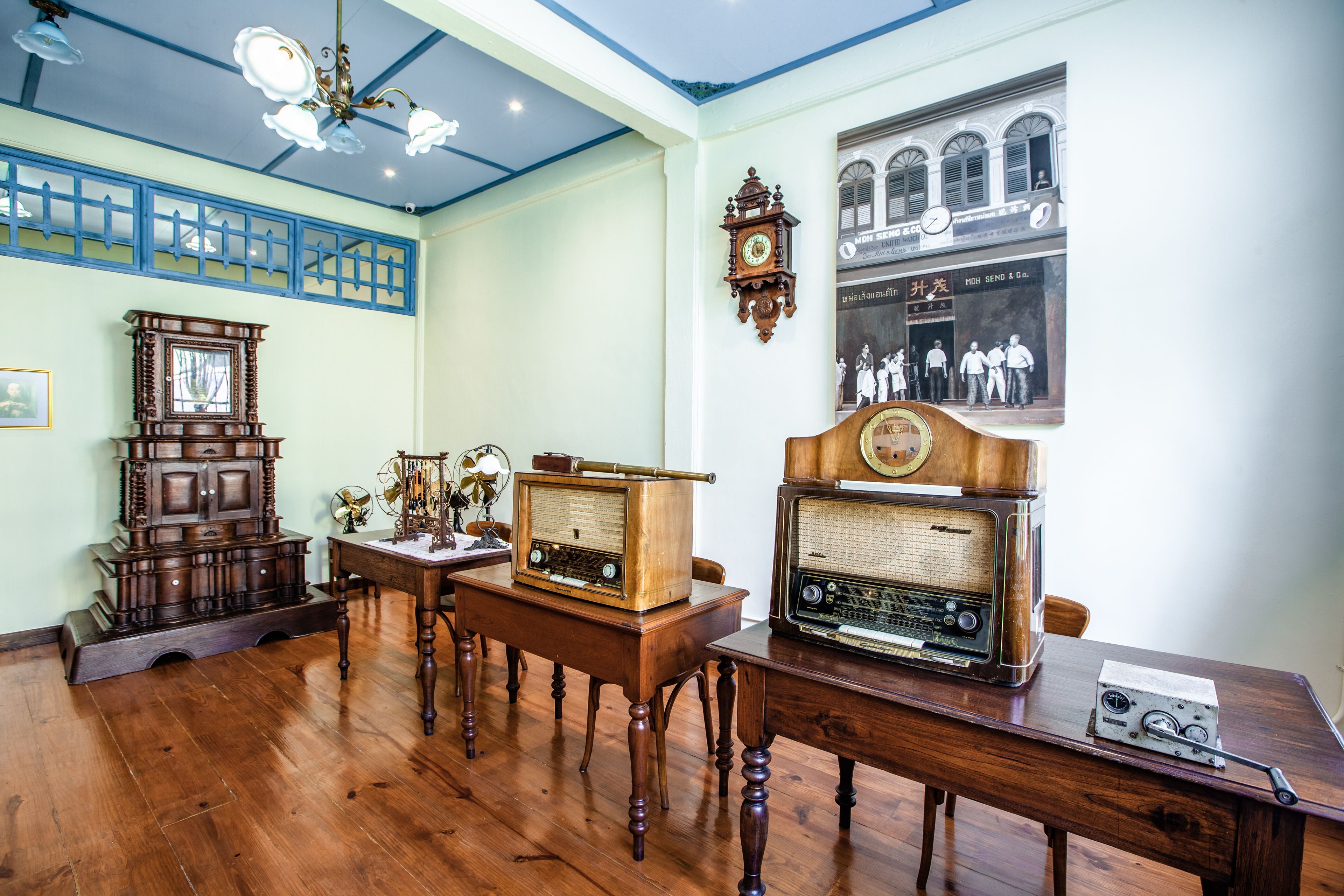 Une pièce meublée de meubles en bois, avec une radio ancienne, une horloge murale et une photographie historique encadrée.