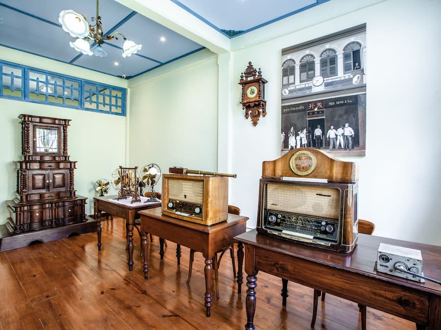 Une pièce meublée de meubles en bois, avec une radio ancienne, une horloge murale et une photographie historique encadrée.