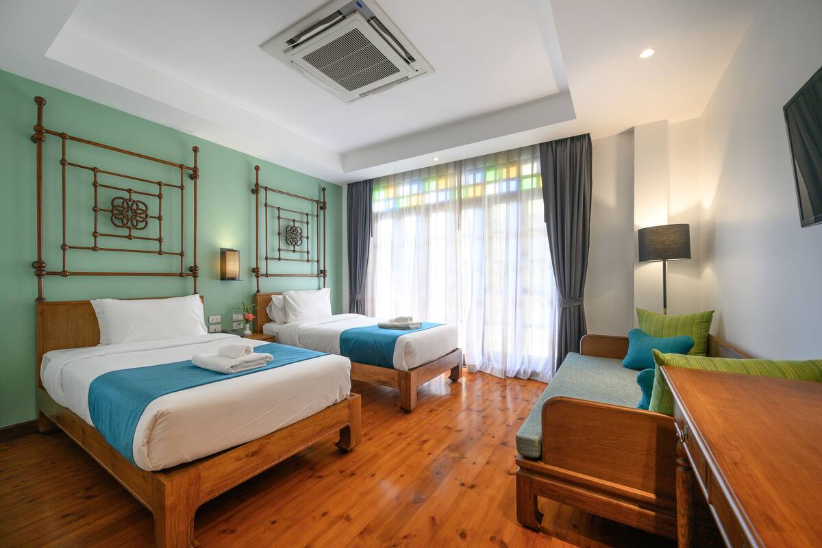 A hotel room with two beds, a wooden floor, a desk, and a chair.