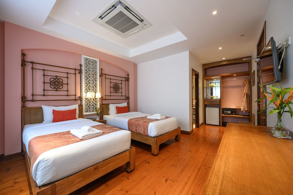 A hotel room with two wooden beds, a wooden dining table, a TV mounted on the wall, and a small kitchenette.