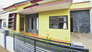A residential building with a yellow facade, a red roof, and a stone wall. - Villa Batu 2 kamar 5 dekat Museum Angkut (Batu)