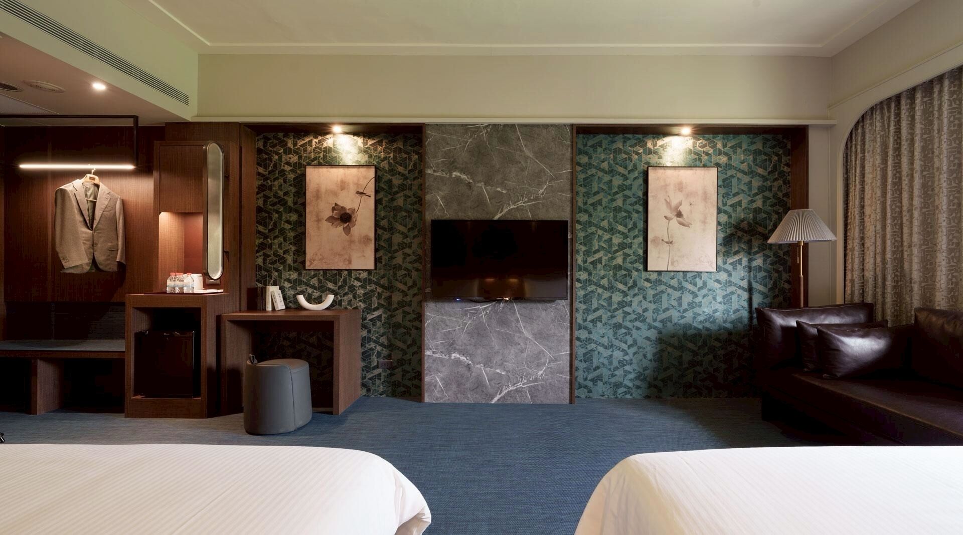 Une chambre d’hôtel avec deux lits, un coin salon, une télévision et des œuvres d’art aux murs.