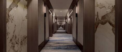 A long, narrow hallway with marble walls and a blue carpet.