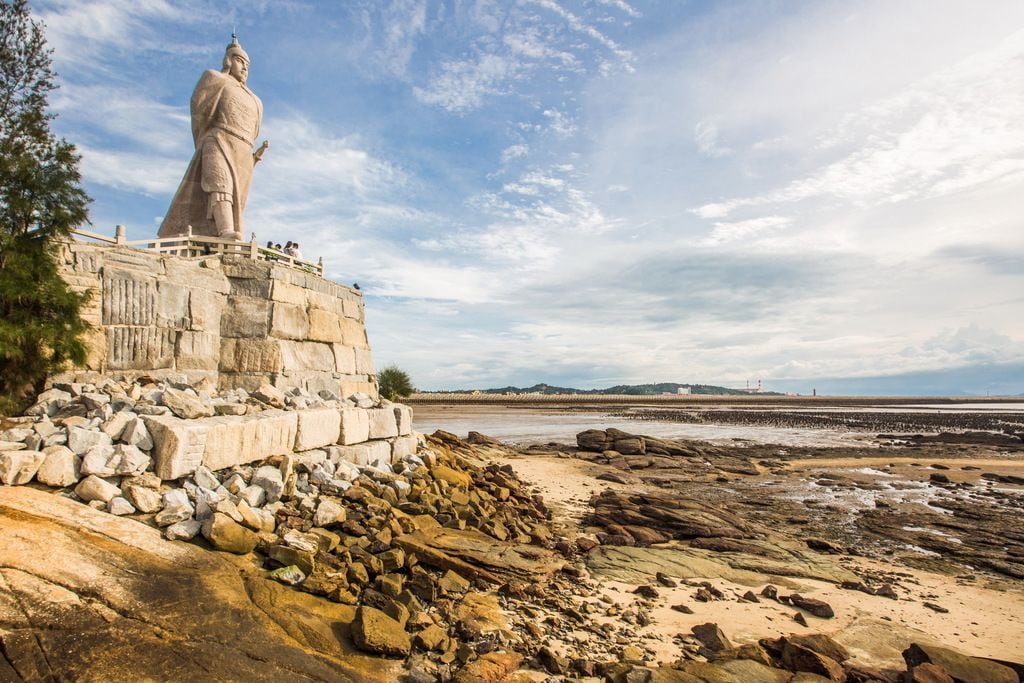 Una estatua de piedra grande sobre una costa rocosa, con cielo despejado.