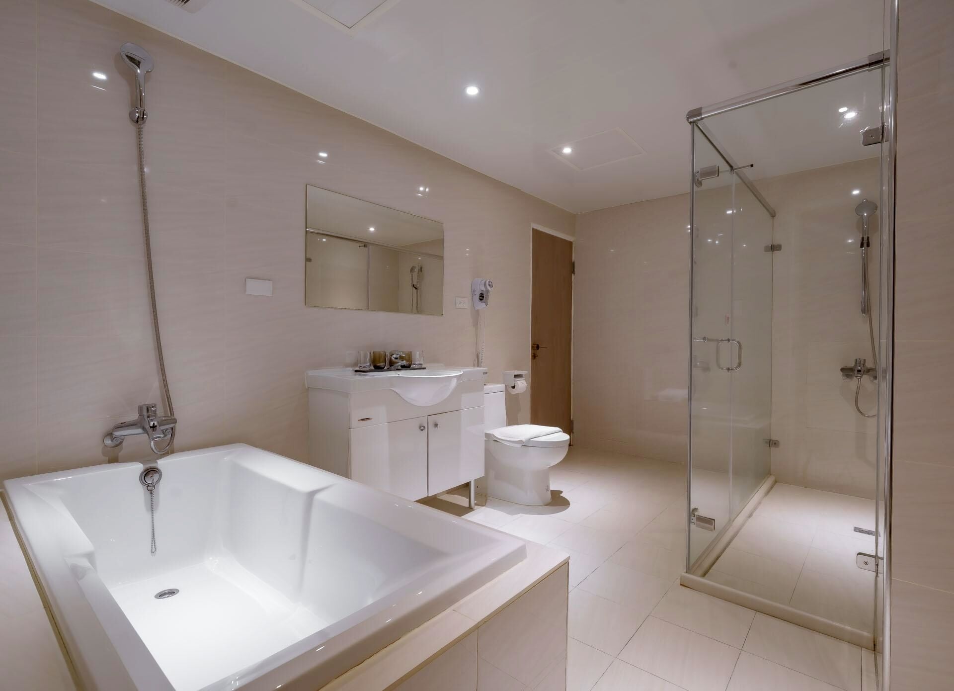 Un baño moderno con una bañera grande, una ducha con mampara de vidrio, un inodoro blanco y un tocador con espejo.
