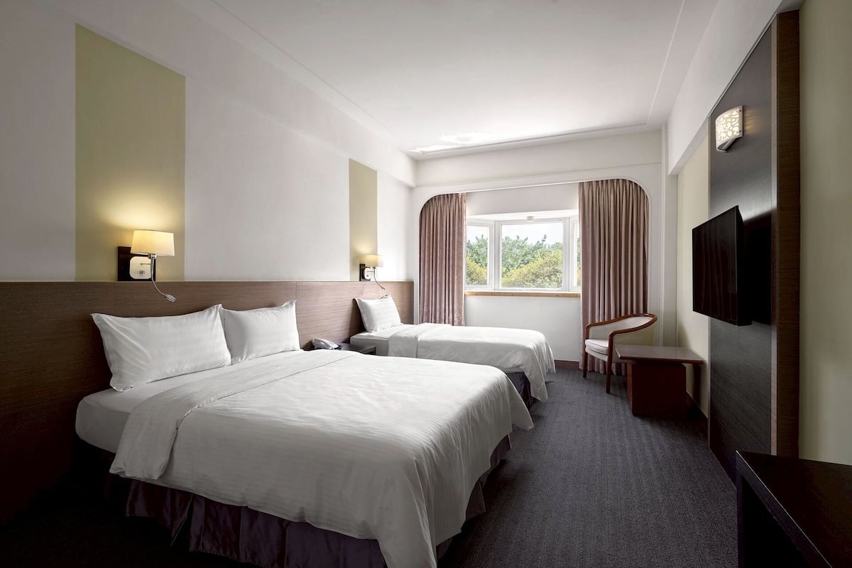 A hotel room with two beds, a desk, a chair, a TV, and a window with curtains.