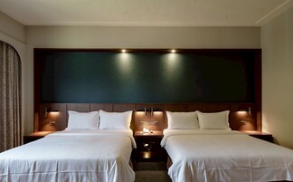 Una habitación de hotel con dos camas, una pared grande de color oscuro e iluminación empotrada.