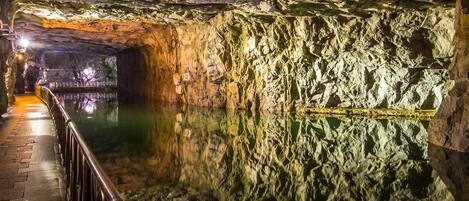 Una cueva con superficie acuática reflectante y una barandilla metálica a lo largo del sendero.
