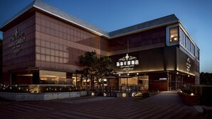 A modern hotel with a large glass facade, outdoor seating area, and illuminated signage. - Haifu Garden Hotel (Jinsha)