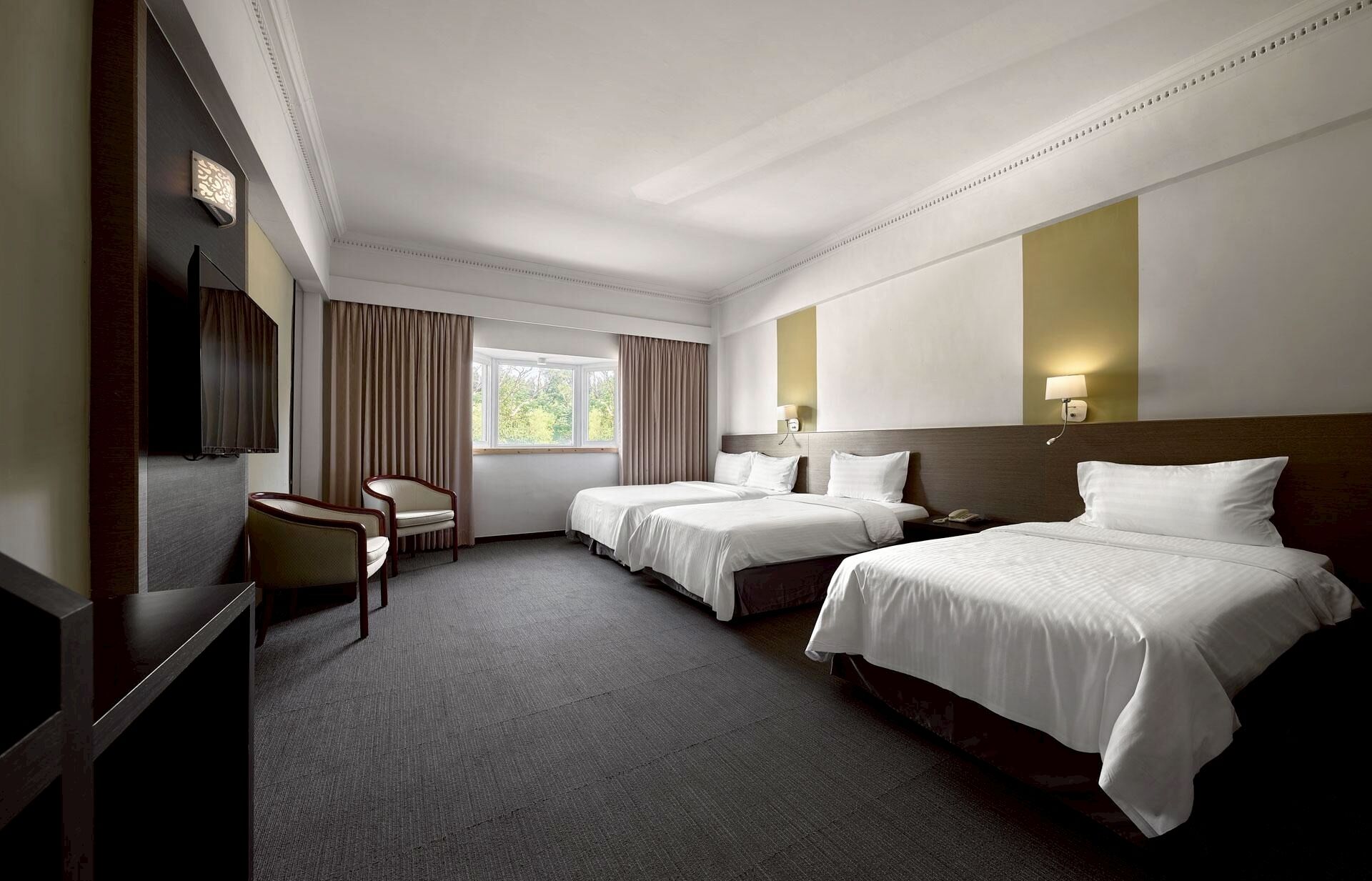 A hotel room with two beds, a desk, a chair, and a TV.