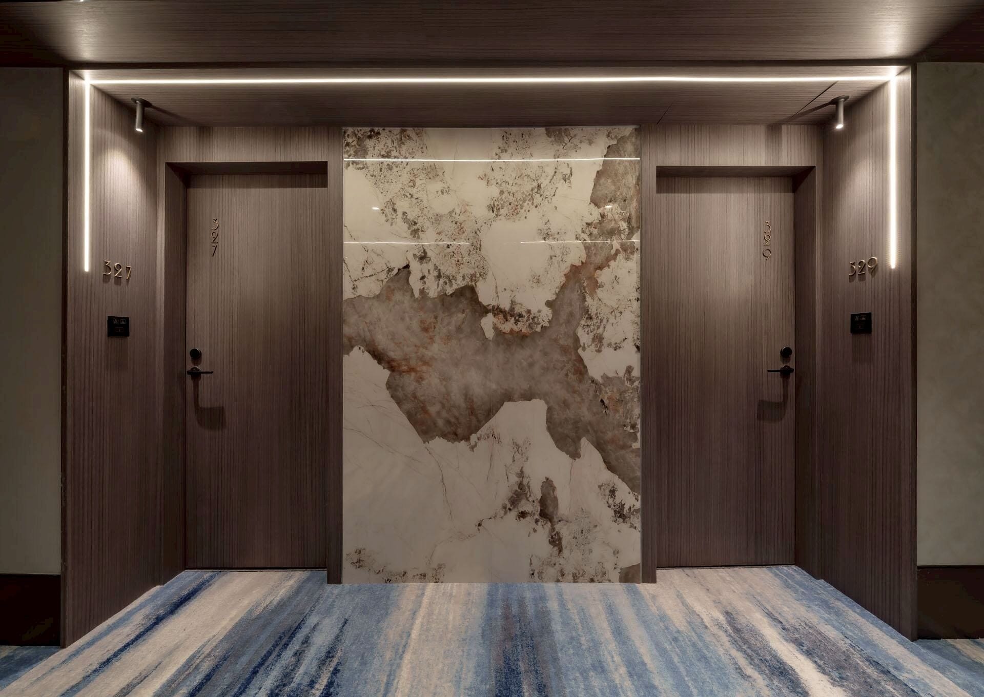 A hotel lobby with a large marble wall, two wooden doors, and a striped carpet.