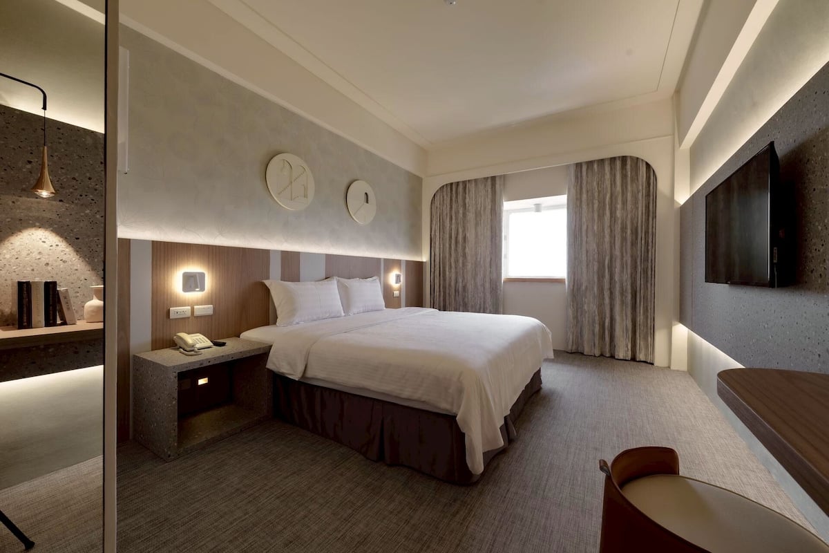 A modern hotel room with a large bed, bedside lamps, a flat-screen TV, and a desk with a telephone.
