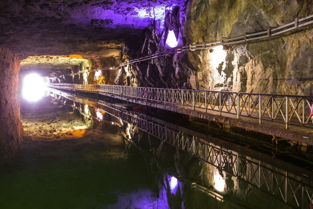 Un puente de metal dentro de una cueva, con una fuente de luz al final.