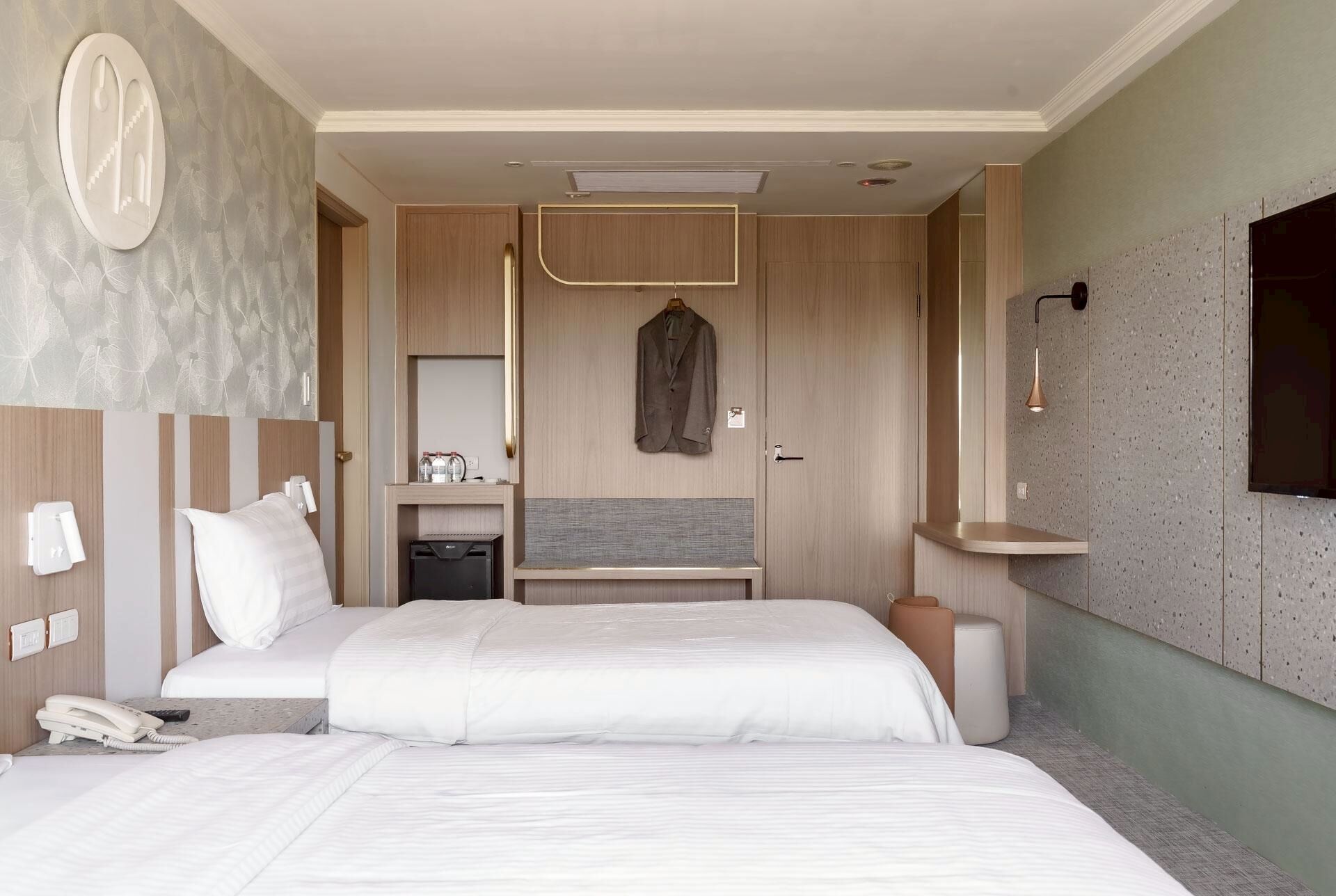 A hotel room with a large bed, bedside tables, a wardrobe, a mirror, and a small desk with a chair.