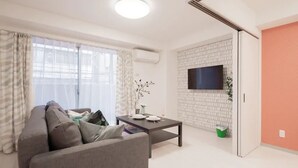 A modern living room with a sofa, a coffee table, and a flat-screen TV mounted on a brick-patterned wall. - Hatch NAGAHORI 201 (Osaka)