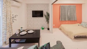 A compact living space with a dining area, a bed, and a TV mounted on the wall. - Hatch NAGAHORI 201 (Osaka)
