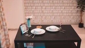 A dining table set with plates, cutlery, and a candle, against a brick-patterned wall with a flat-screen TV mounted above. - Hatch NAGAHORI 201 (Osaka)