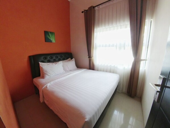 A hotel room with a bed, a headboard, a window with curtains, and a small picture on the wall.