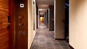A hotel corridor with a wooden door on the left, tiled flooring, and a series of doors along the corridor. - The Batu Villas No 2 near Jatim Park (Batu)