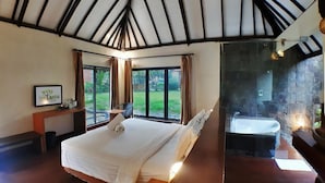 A bedroom with a large bed, a desk, a chair, a bathtub, and a view of the outdoors. - The Batu Villas No 2 near Jatim Park (Batu)