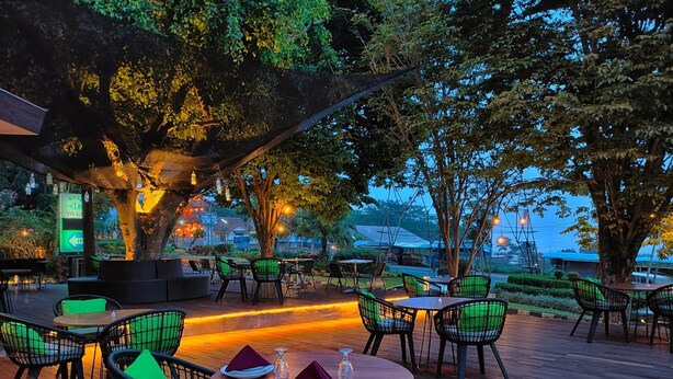 An outdoor dining area with round tables and chairs, surrounded by trees and illuminated by string lights. - The Batu Villas No 2 near Jatim Park (Batu)