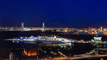 Un paisaje urbano nocturno con un puente destacado, un gran barco de crucero amarrado en un puerto y edificios iluminados.