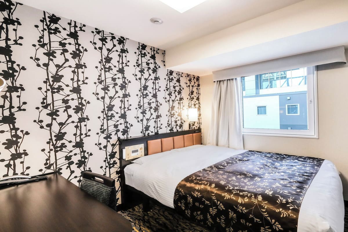 Ein Hotelzimmer mit einem Bett, einem Schreibtisch, einem Sessel, einem Fernseher und einem Fenster mit Blick auf Gebäude.