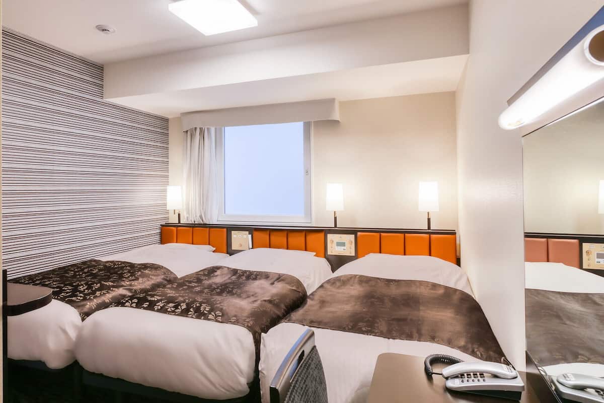 Ein Hotelzimmer mit zwei Betten, einem Fenster, einem Nachttisch mit Telefon und einem Kopfteil mit Bedienfeld.
