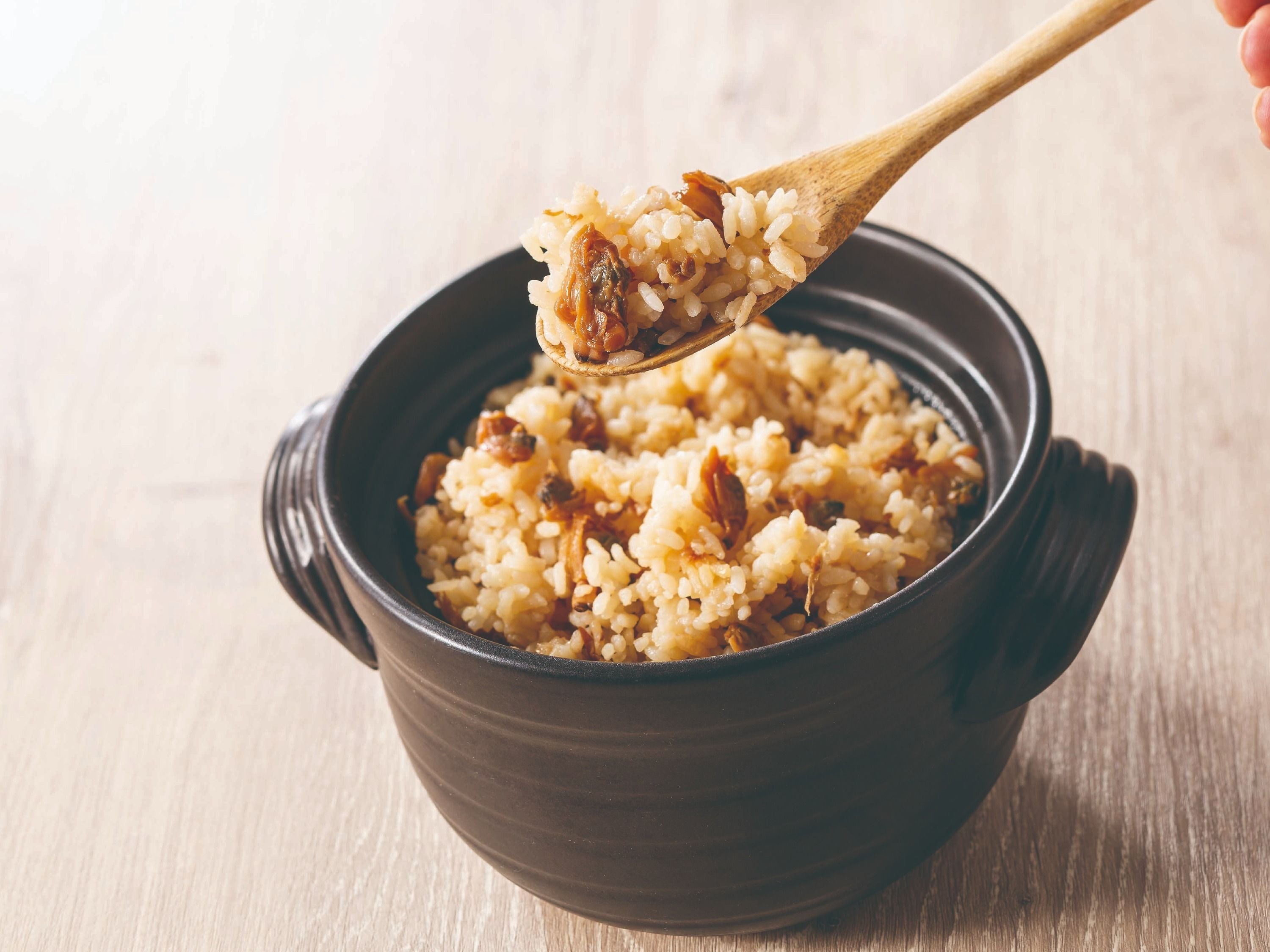 A bowl of rice with raisins being lifted by a wooden spoon.