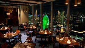 A restaurant with tables set for dining, large windows offering a city view, and hanging pendant lights. - APA Hotel & Resort Yokohama Bay Tower (Yokohama)