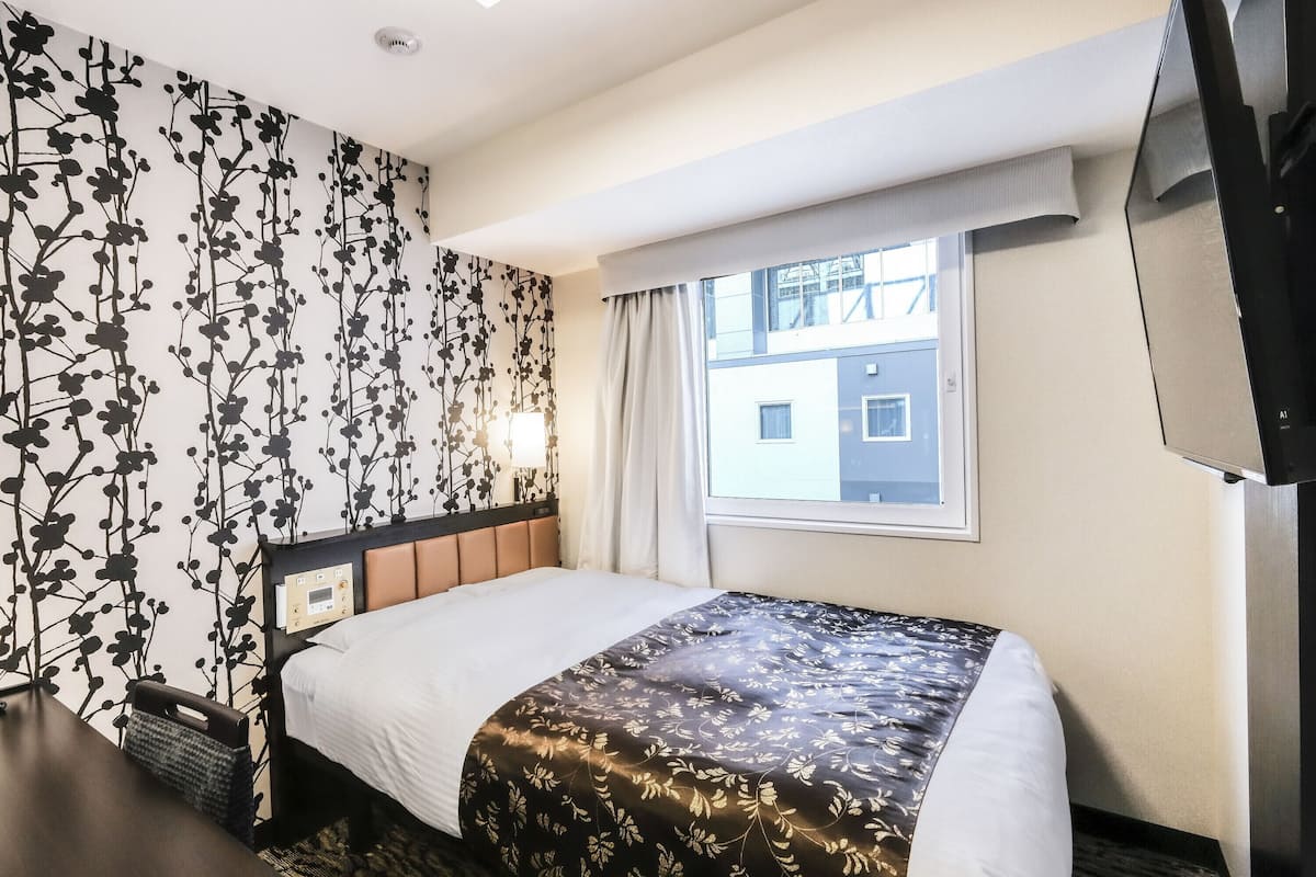 Ein Hotelzimmer mit Bett, Fernseher, Fenster und einer Wand mit floralem Muster.
