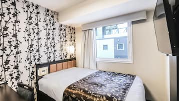 A hotel room with a bed, a TV, a window, and a wall with a floral pattern.