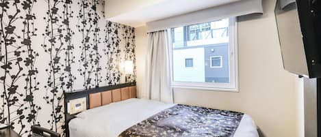 A hotel room with a bed, a TV, a window, and a wall with a floral pattern.