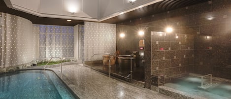 A modern indoor pool area with a long, rectangular pool, a separate hot tub, and a sauna area.