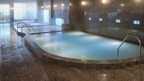 A large indoor swimming pool with a curved design, surrounded by stone walls and equipped with metal ladders.