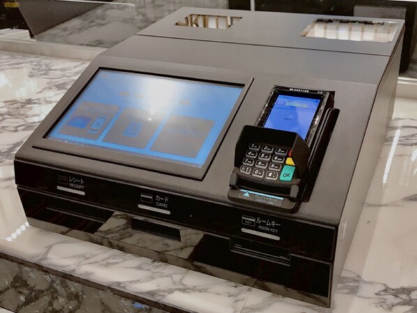 Una moderna recepción de hotel con una pantalla digital, un lector de tarjetas y un pequeño dispositivo para acceder a las llaves de las habitaciones.