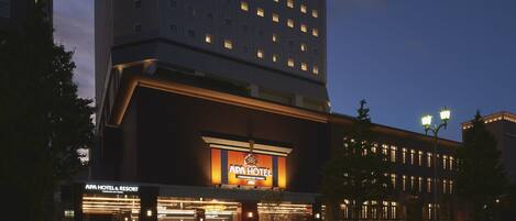 A modern hotel with a prominent sign for APA Hotel & Resort, featuring a large entrance and a well-lit facade.