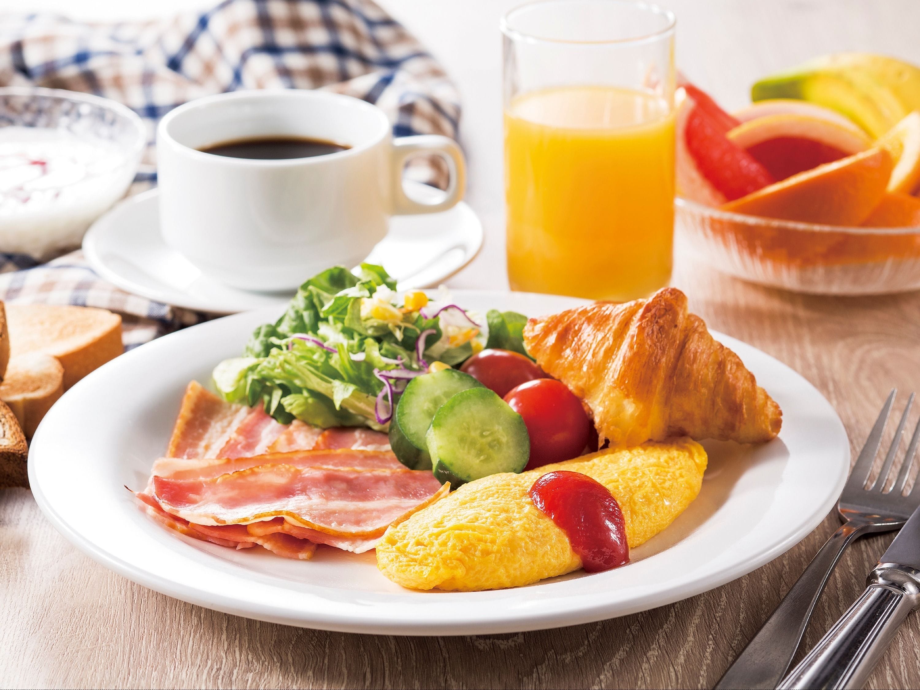 Prato de pequeno-almoço com fiambre, ovos, um croissant e uma salada.