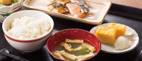 Una bandeja con un bol de arroz blanco, un bol de sopa de tofu, un plato con pescado y verduras, y un plato con cubos de tofu y un bollo.