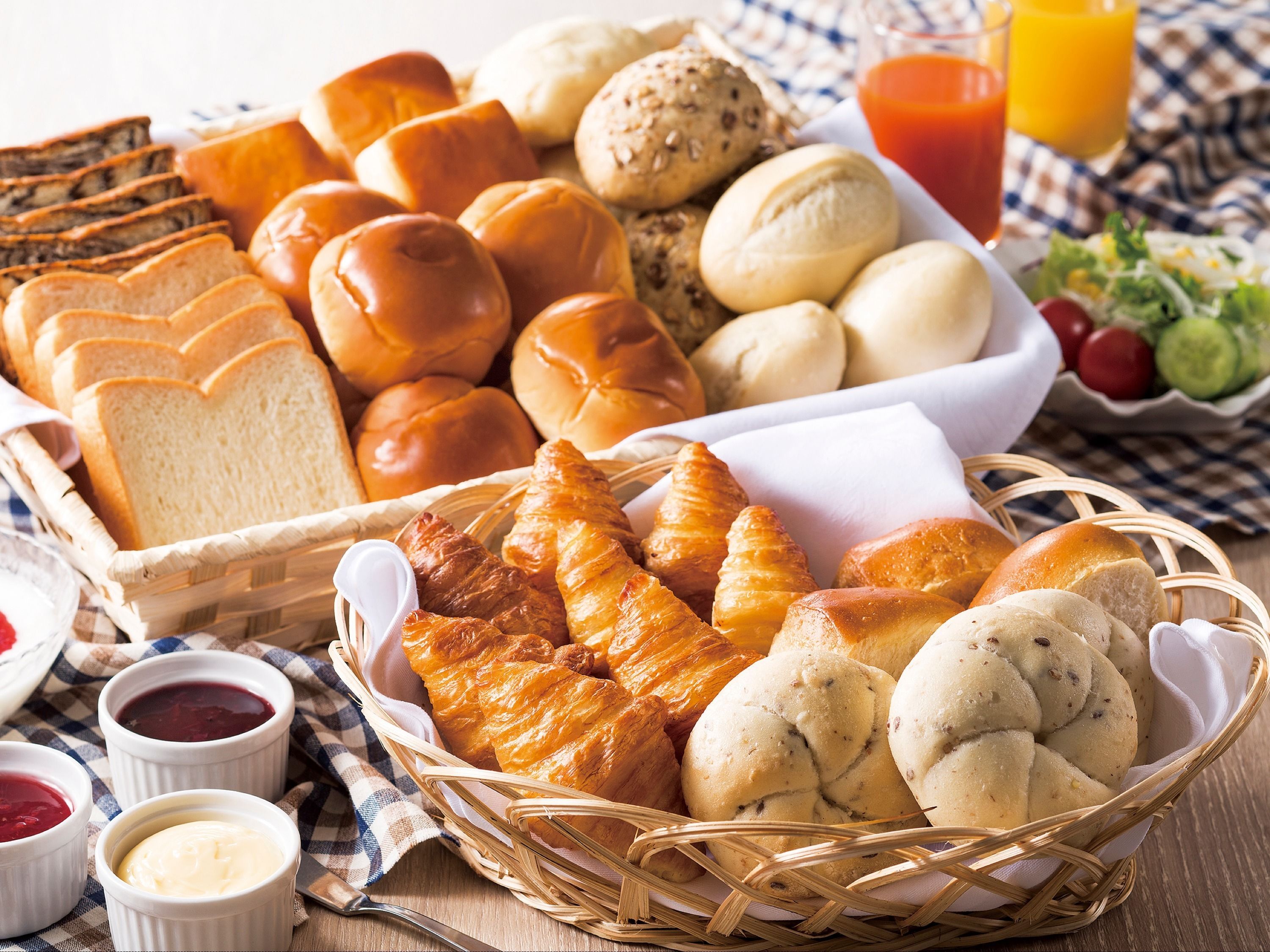 En kurv med forskellige brød og kager, blandt andet croissanter og rundstykker, samt små skåle med tilbehør.