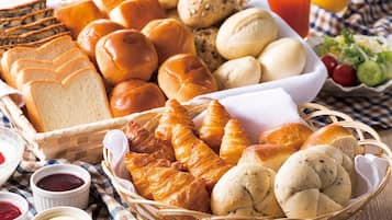 En kurv med forskellige brød og kager, blandt andet croissanter og rundstykker, samt små skåle med tilbehør.